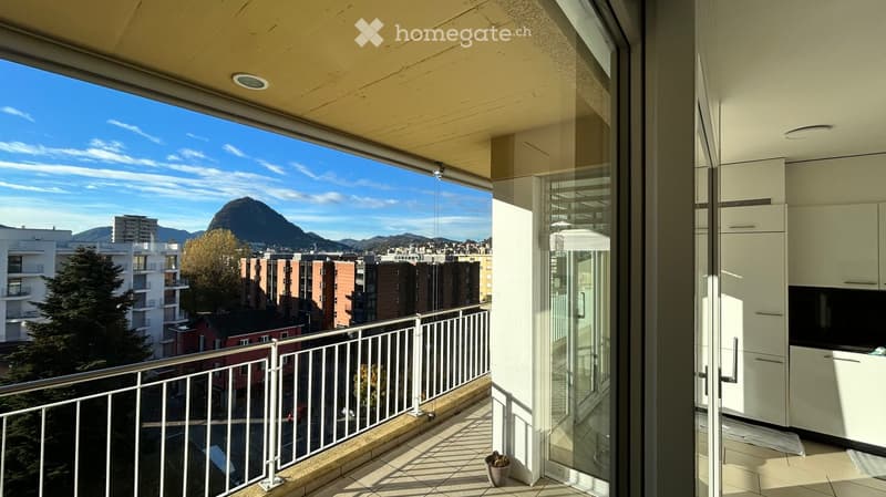 Balcony with a view of a cityscape and mountains, featuring a metal railing and tiled floor.