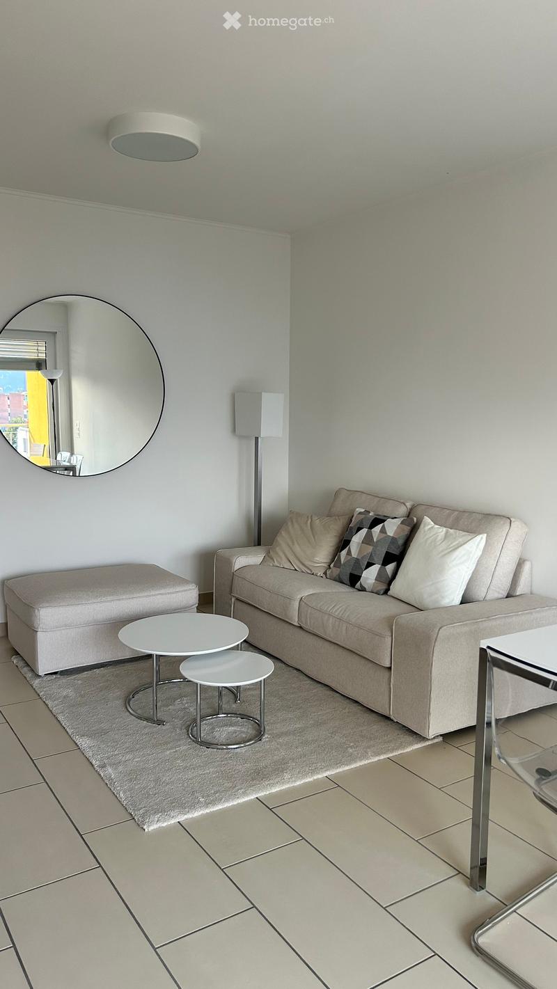 Modern living room with a beige sofa, two small white tables, a round mirror, and a floor lamp.
