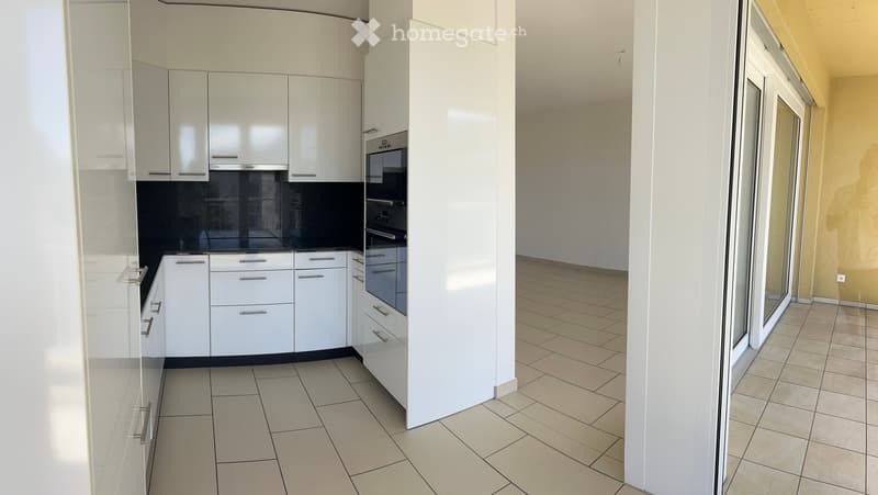 White cabinets, tiled flooring, black countertop, two ovens, open sliding glass door