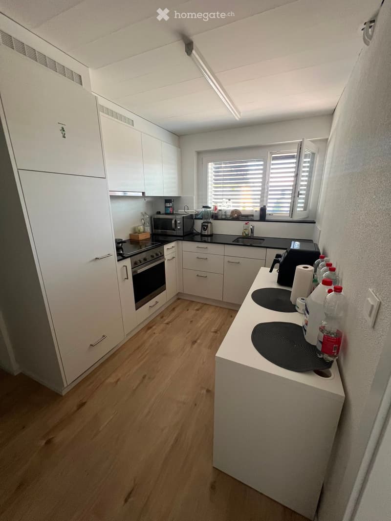 Modern kitchen with white cabinets, wooden flooring, and various appliances including an oven, microwave, and induction cooktop.