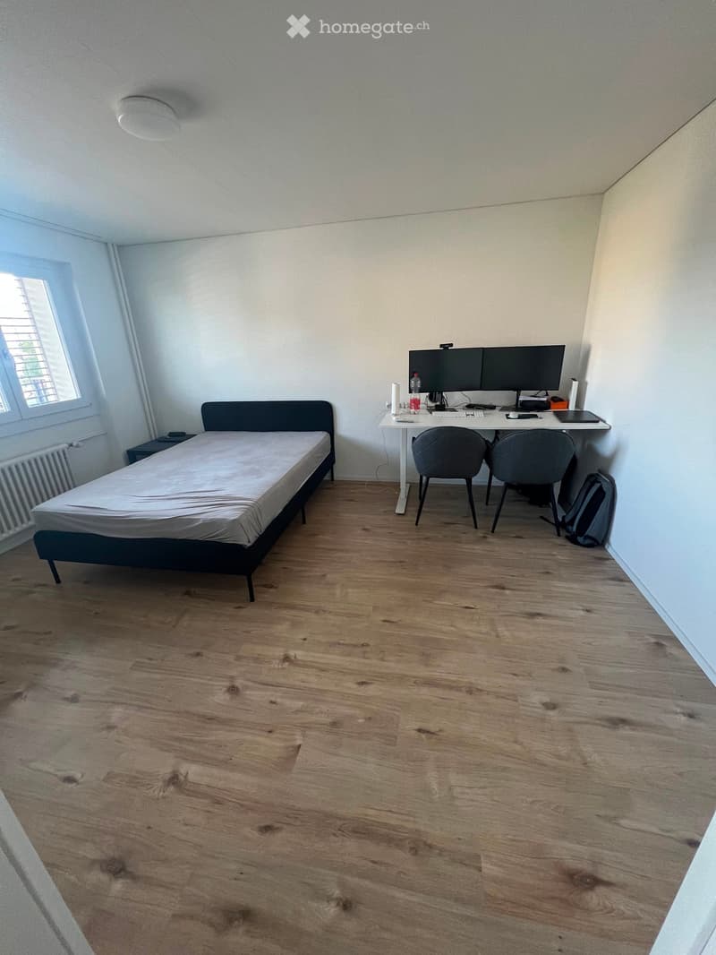 A furnished bedroom with a single bed, a desk with two monitors, two chairs, and a backpack placed near the desk.