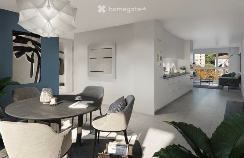 Modern open-plan living and dining area with a round wooden dining table, four chairs, white kitchen cabinets, a sink, and a potted plant. A sofa and a table lamp are visible in the background, along with an art piece on the wall.