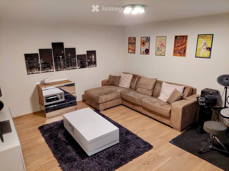 Modern living room with a large sectional sofa, coffee table, drum set, and decorative artwork on the walls.