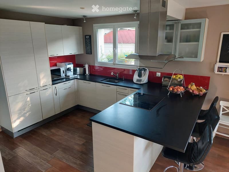 Modern kitchen with white cabinets, black countertops, a central island, and various appliances including a microwave, coffee maker, and blender. The island features a black countertop and a built-in induction cooktop. There are two black bar stools and a