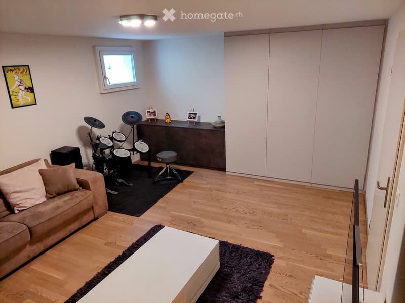 Living room with wooden flooring, a sofa, coffee table, drum set, and a cabinet with decorative items.