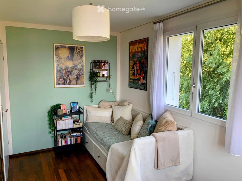 Cozy, well-lit room with a built-in window seat sofa, bookshelves, artwork, and a pendant light.