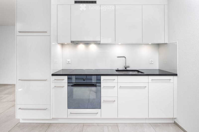 Modern kitchen with white cabinets, stainless steel handles, a black countertop, a sink with a modern faucet, and a built-in oven.
