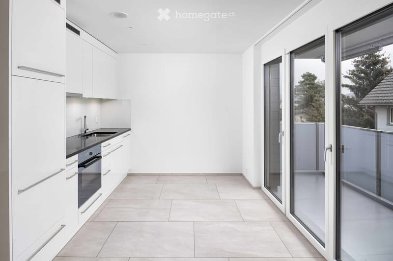 Modern, minimalist kitchen with white cabinets, a black countertop, and a sink. Large glass sliding doors lead to a balcony.