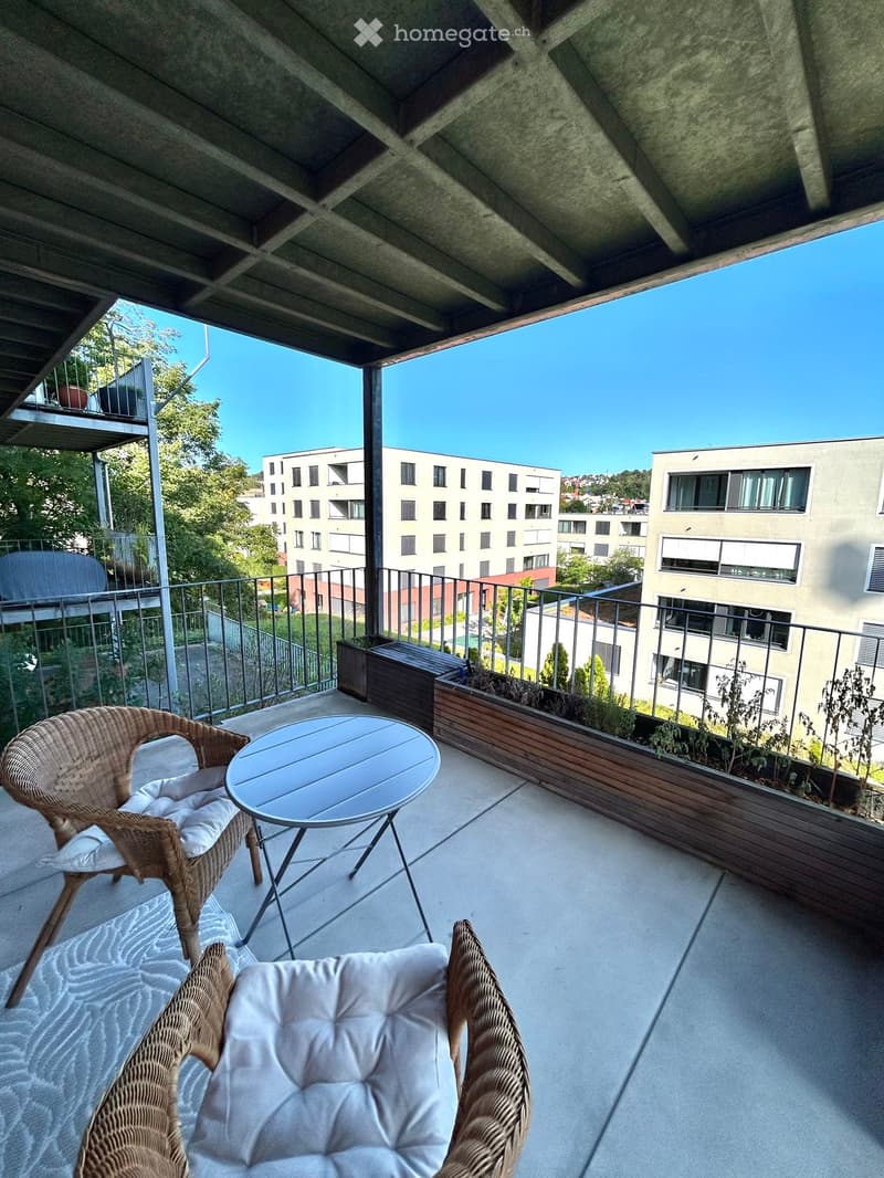 Balcony with a round table, two wicker chairs, and a view of the cityscape.