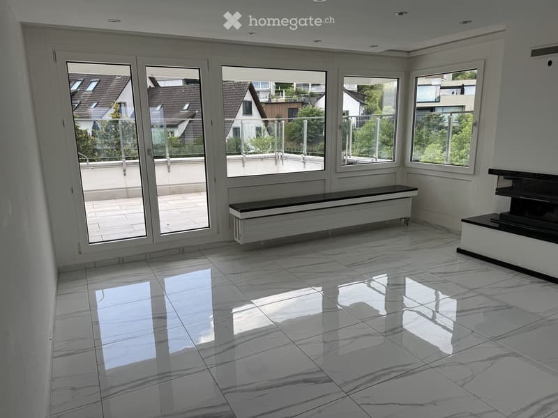 Empty room with white marble flooring, large windows, and a balcony view of neighboring houses and greenery.