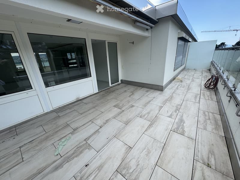 Modern rooftop terrace with polished stone tiles, large glass windows, and a sleek metal railing.