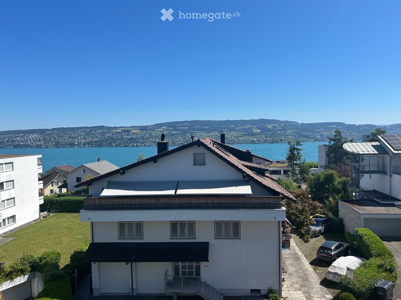 A two-story house with a white exterior, multiple windows, a garage, and a well-maintained lawn. The house is situated near a lake with a scenic view of the surrounding landscape.