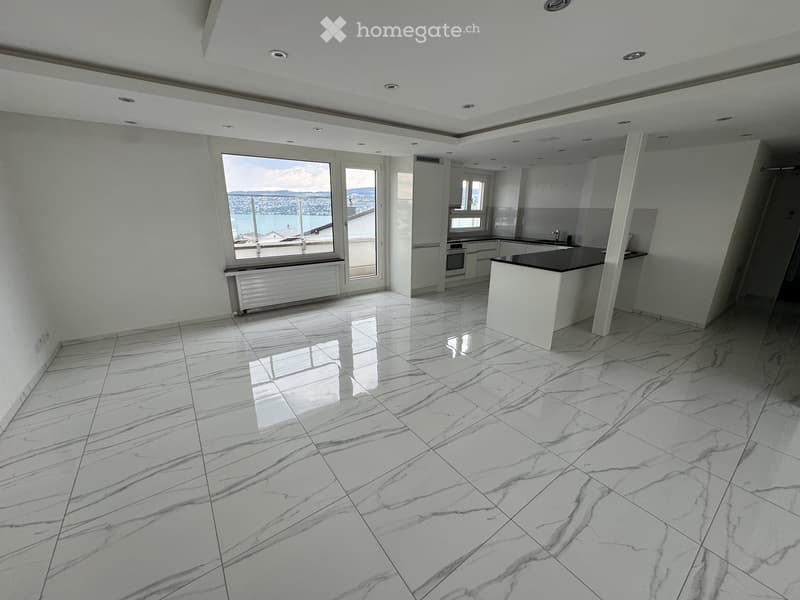 Modern kitchen with white marble flooring, white cabinets, a central island, and large windows offering a view of the water.