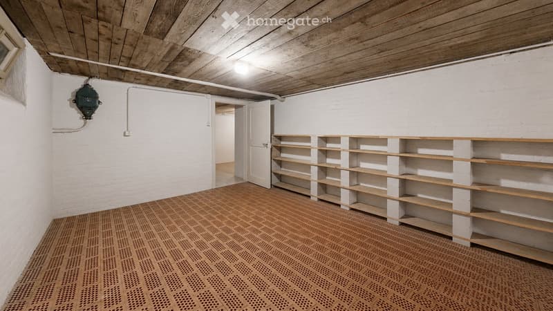 Empty room with white brick walls, wooden ceiling, and built-in wooden shelving unit. The floor is covered with a patterned, perforated wooden mat.