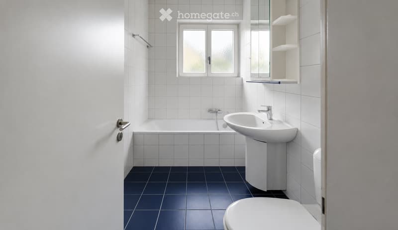 Modern bathroom with white tiled walls, dark grey floor tiles, a bathtub, a sink, a toilet, and a mirrored cabinet.