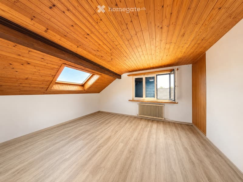 Empty room with wooden flooring, white walls, wooden ceiling, and large windows including a skylight. Radiator visible under one window.
