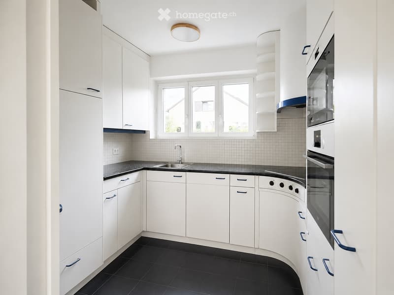 Modern kitchen with white cabinets, black countertop, sink, and built-in oven. Features a large window and recessed lighting.