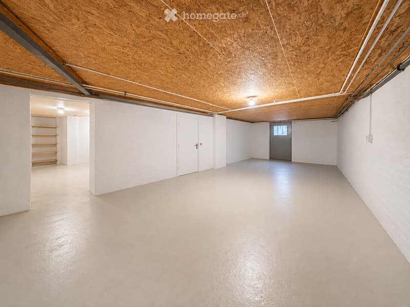 Empty garage with white brick walls, concrete floor, exposed wooden ceiling, and a single door leading outside.