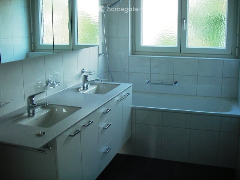 Modern bathroom with two sinks, a bathtub, and white tiled walls and cabinets.