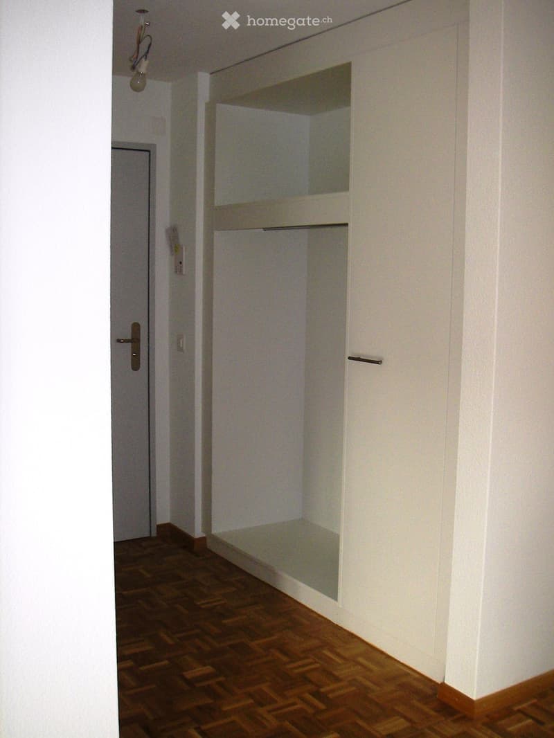 Empty hallway with wooden flooring, white walls, and a built-in closet with mirrored doors.
