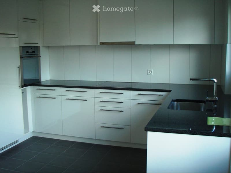 Modern kitchen with white cabinets, black countertops, and a stainless steel sink.