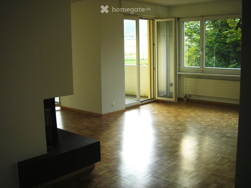 Empty room with wooden flooring, large windows, and sliding glass doors leading to a balcony.