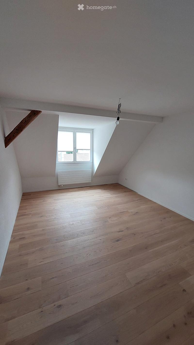 Empty attic room with wooden flooring, white walls, and a skylight window. No furniture or equipment present.
