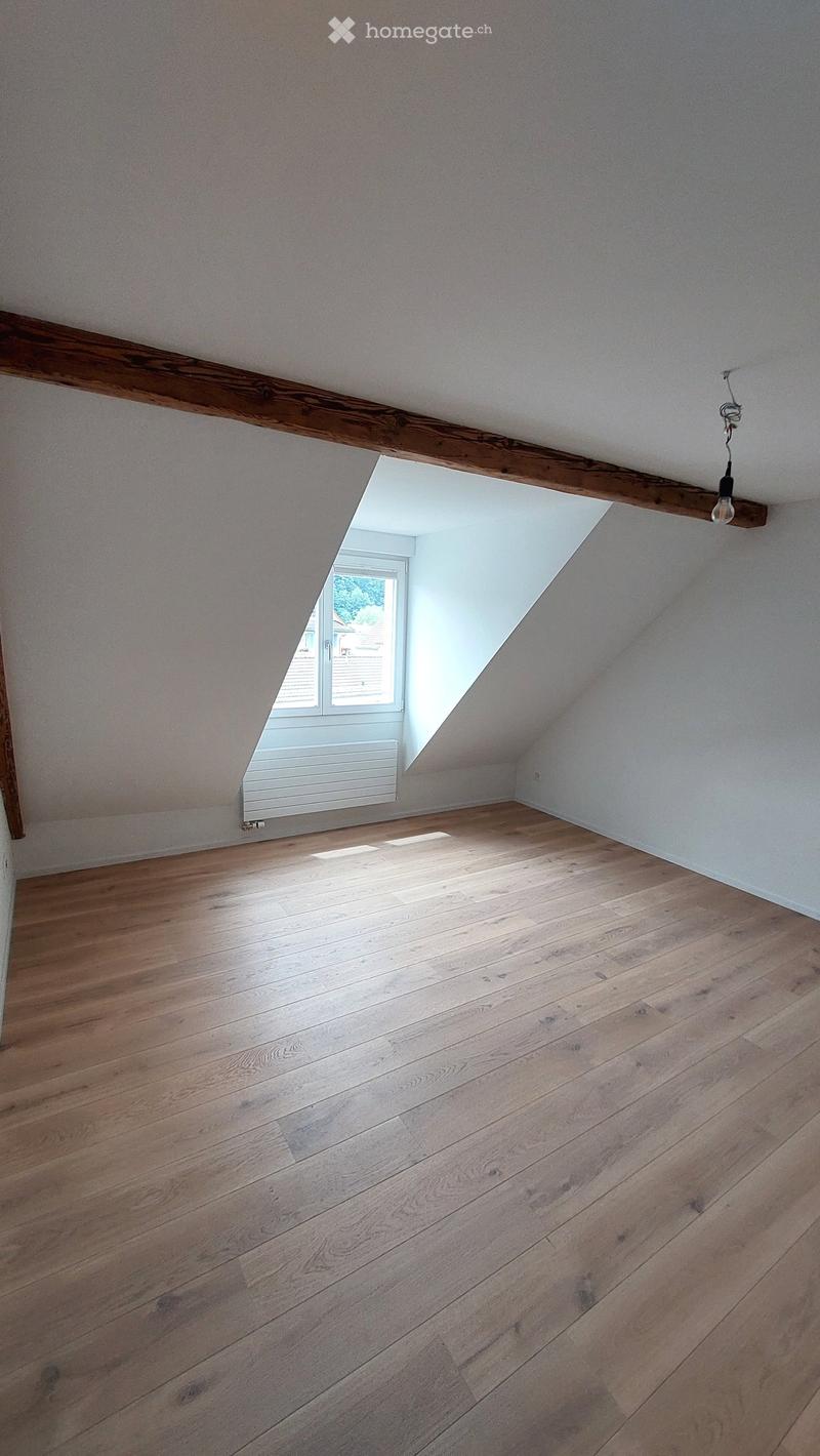 Empty attic room with wooden floor, exposed wooden beam, skylight window, and white radiator.