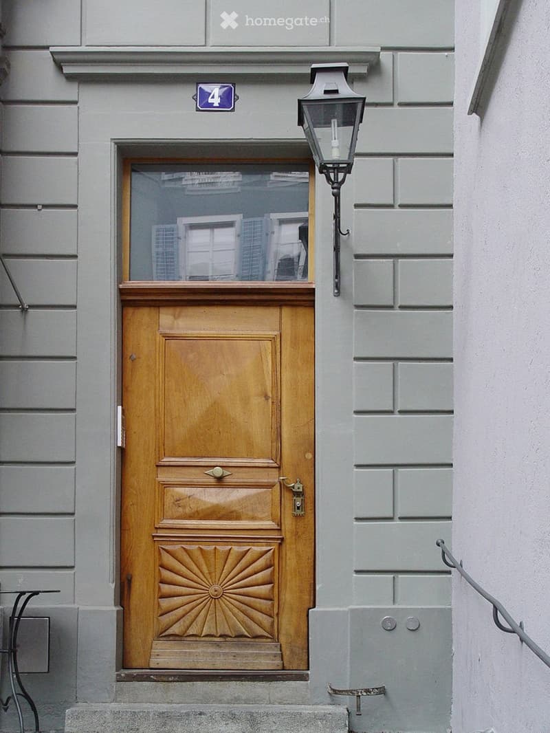 Wooden front door with decorative panels, glass window above, and a lantern-style light fixture mounted on the wall.