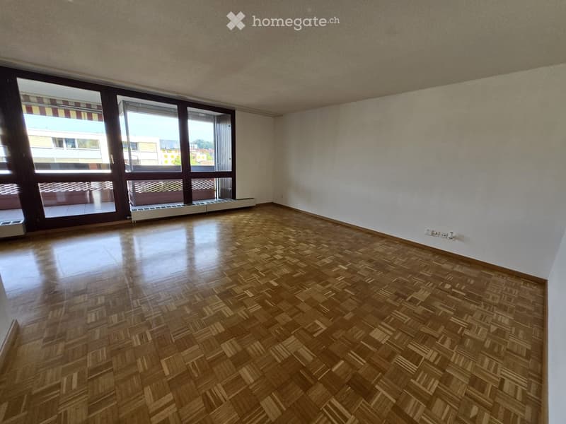 Empty room with wooden parquet flooring, white walls, large windows with blinds, and a radiator under the windows.