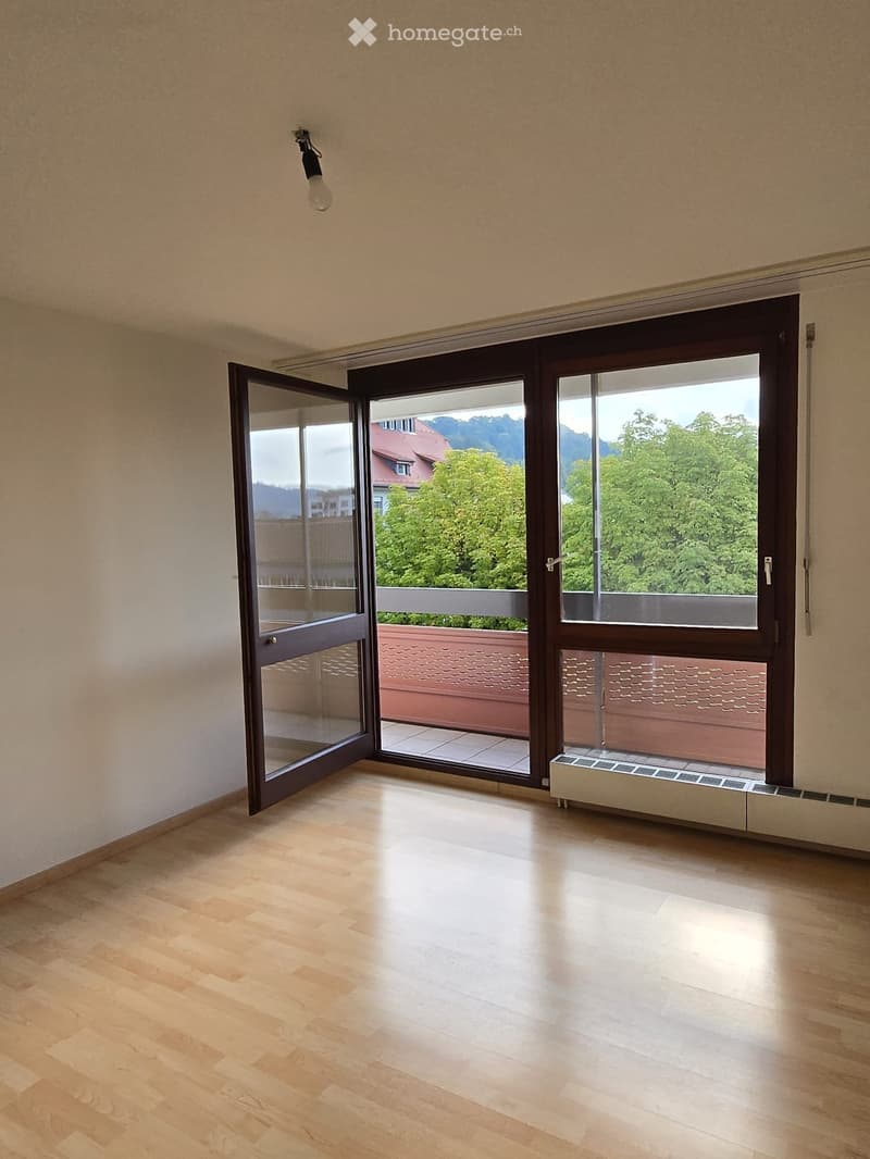 Empty room with wooden flooring, large sliding glass doors opening to a balcony, and a radiator below the window.