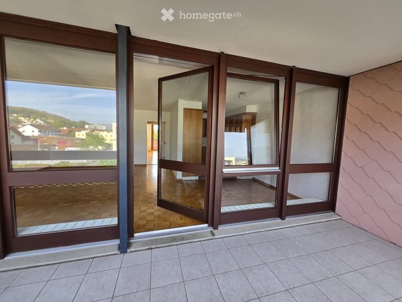 Balcony with large sliding glass doors leading to an interior space, tiled floor, and a view of a town and hills.