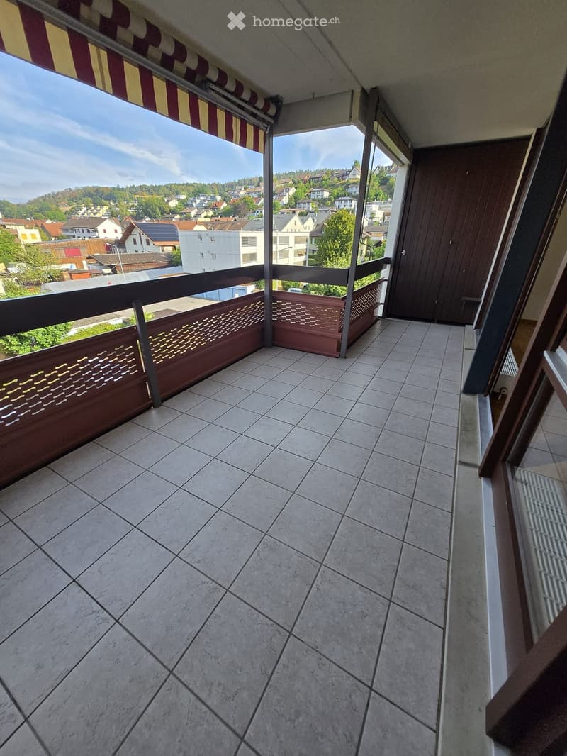 Balcony with tiled floor, wooden railing, and scenic view of a town with houses and greenery.