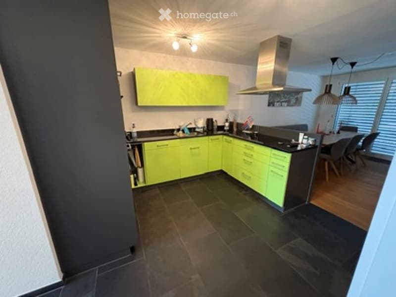 Modern kitchen with bright green cabinets, black countertops, and a dining area with a table and chairs.