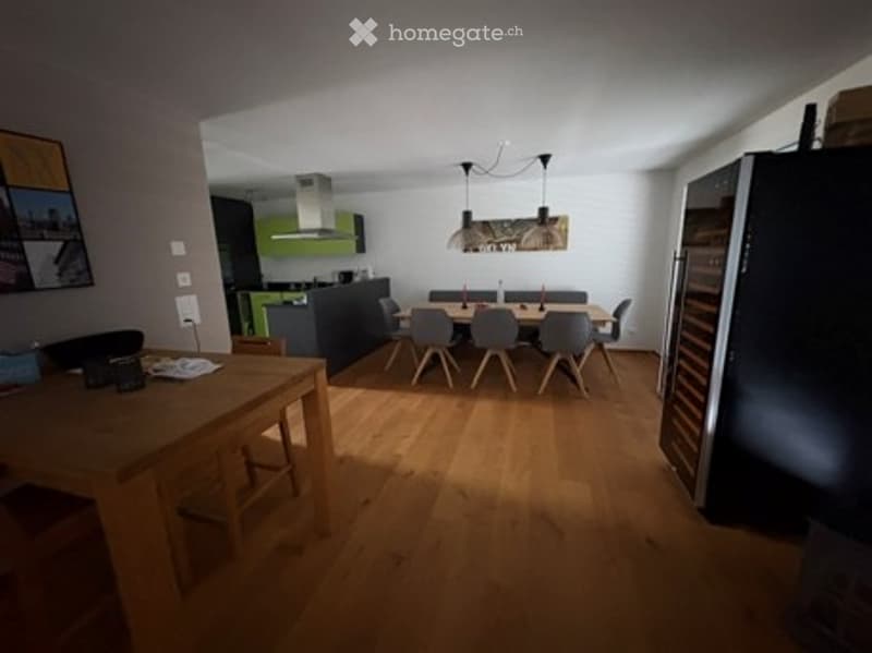 Bright, open-plan dining and kitchen area with wooden flooring, modern kitchen cabinets, a dining table with chairs, and a refrigerator.