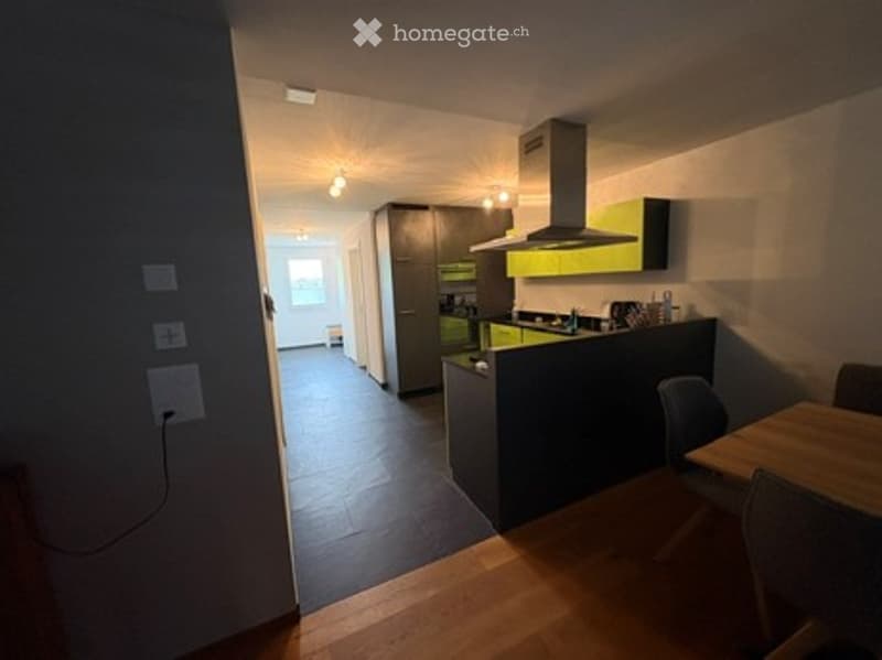 Modern kitchen with dark green cabinets, stainless steel appliances, and a wooden dining area with a table and chairs.