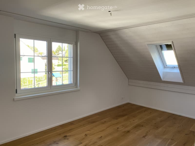 Empty room with wooden flooring, white walls, and two windows, one of which is a skylight.