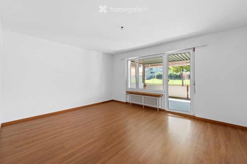 Empty room, wooden floors, white walls, sliding glass doors to balcony, white radiator