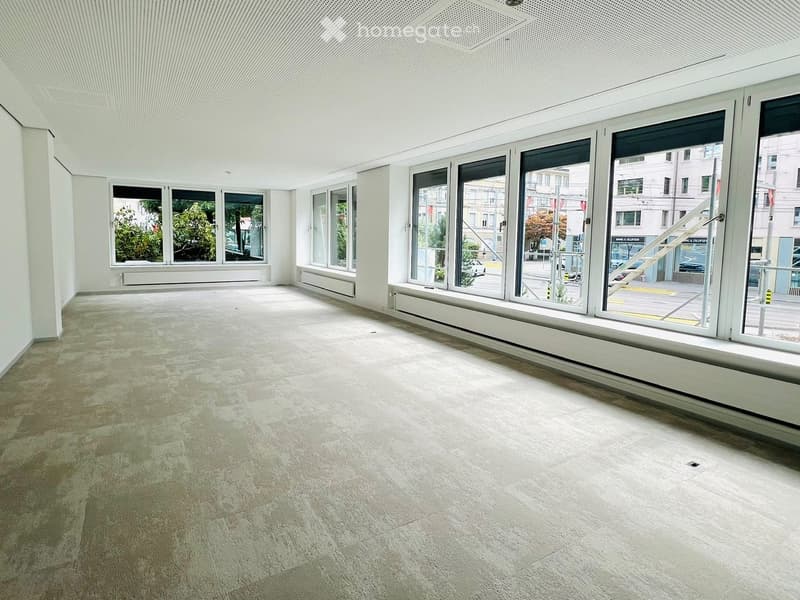 Empty room with large windows, light-colored carpeted floor, white walls, and a modern ceiling design.