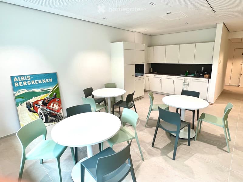 Bright, modern room with white cabinets, a sink, and three round tables surrounded by colorful chairs.