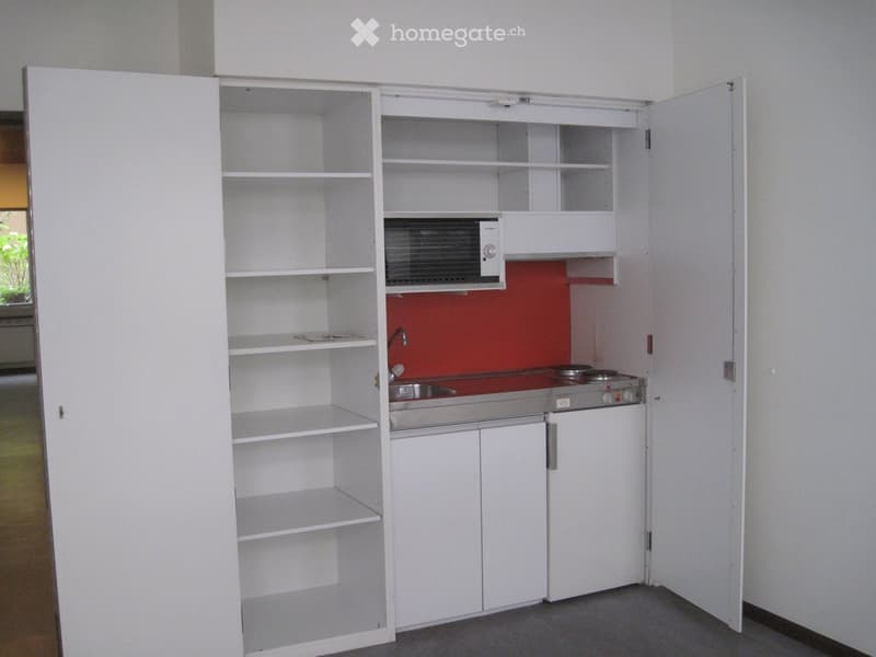 Compact kitchen with white cabinets, a sink, a stove, and a microwave. The cabinets are open, revealing empty shelves.