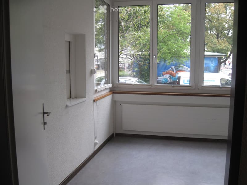 Empty room with white walls, carpeted floor, large windows with wooden sills, and a radiator below the windows.