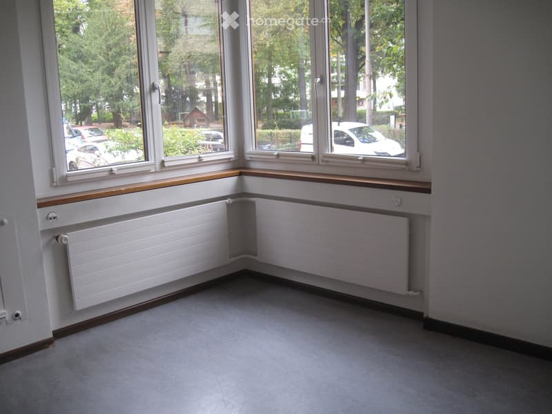 Empty room with large windows, wooden window sills, radiators, and grey carpeted floor.