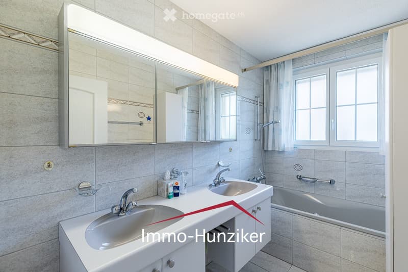 Modern bathroom with double sink, bathtub, large mirror, and window with curtain.