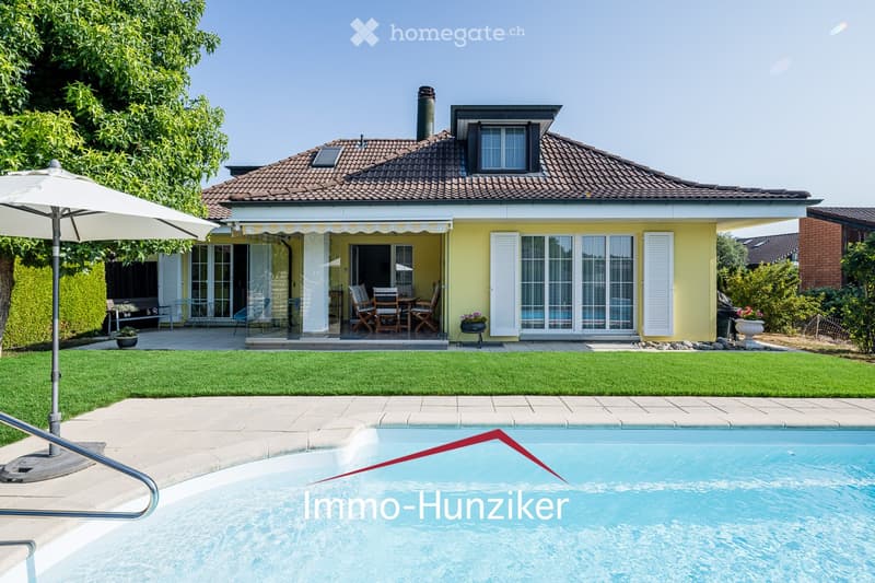 Single-story yellow house with a tiled roof, surrounded by a well-maintained lawn, patio furniture, and a swimming pool.