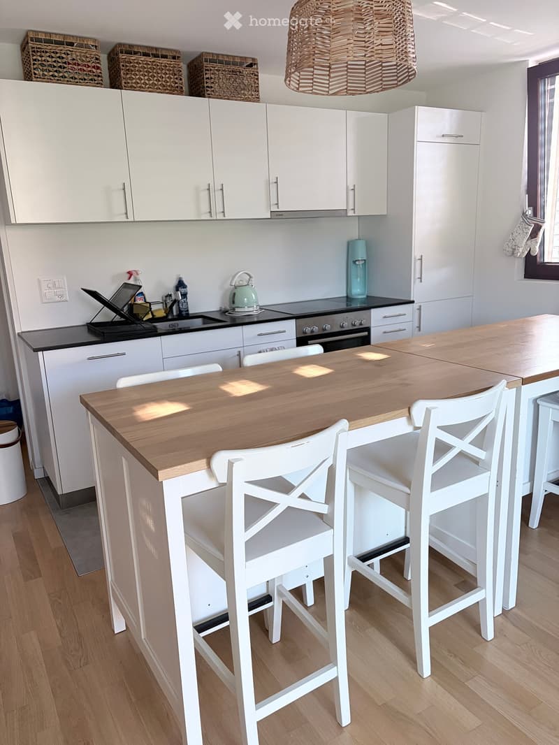 Modern kitchen with white cabinets, a wooden island, white stools, and various appliances including an oven and a faucet.
