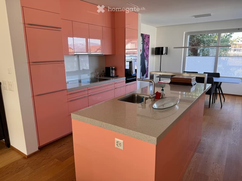 Modern kitchen with pink cabinets, granite countertop, stainless steel sink, coffee maker, and dining area with chairs and table.