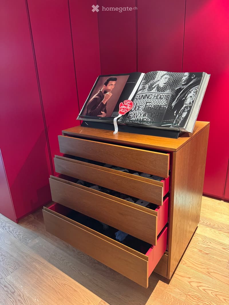A wooden table with multiple drawers, a book on top, and a red accent wall in the background.