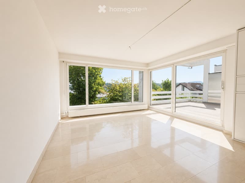 Bright, empty room with large windows and sliding glass doors leading to a balcony. Light-colored tiled floor and white walls.