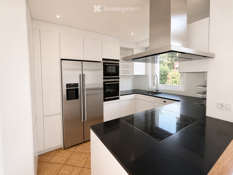 Modern kitchen with white cabinets, stainless steel appliances, black countertop, and an induction cooktop.